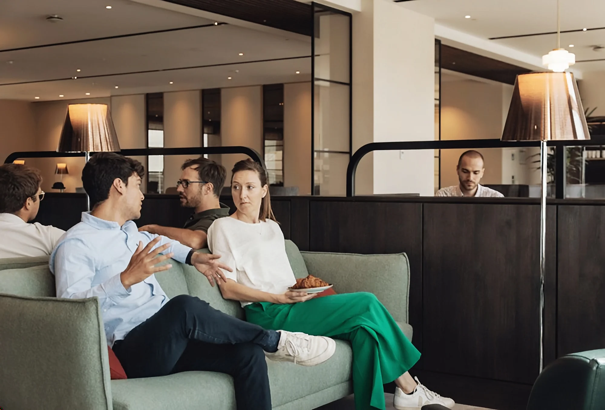 Freunde sitzen zusammen auf dem Sofa der The View Lounge am Flughafen Brüssel, eine Frau hält einen Teller mit Croissant