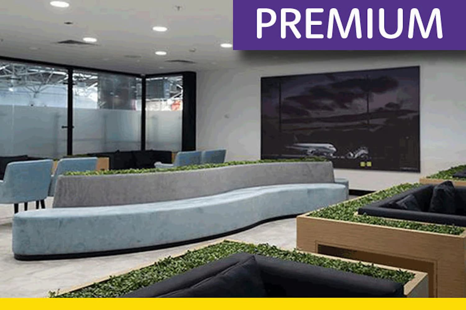 Geschwungene hellblaue und graue Sitzbänke mit Pflanzkästen vor großen Fenstern in der Comfort Lounge am Flughafen Antalya