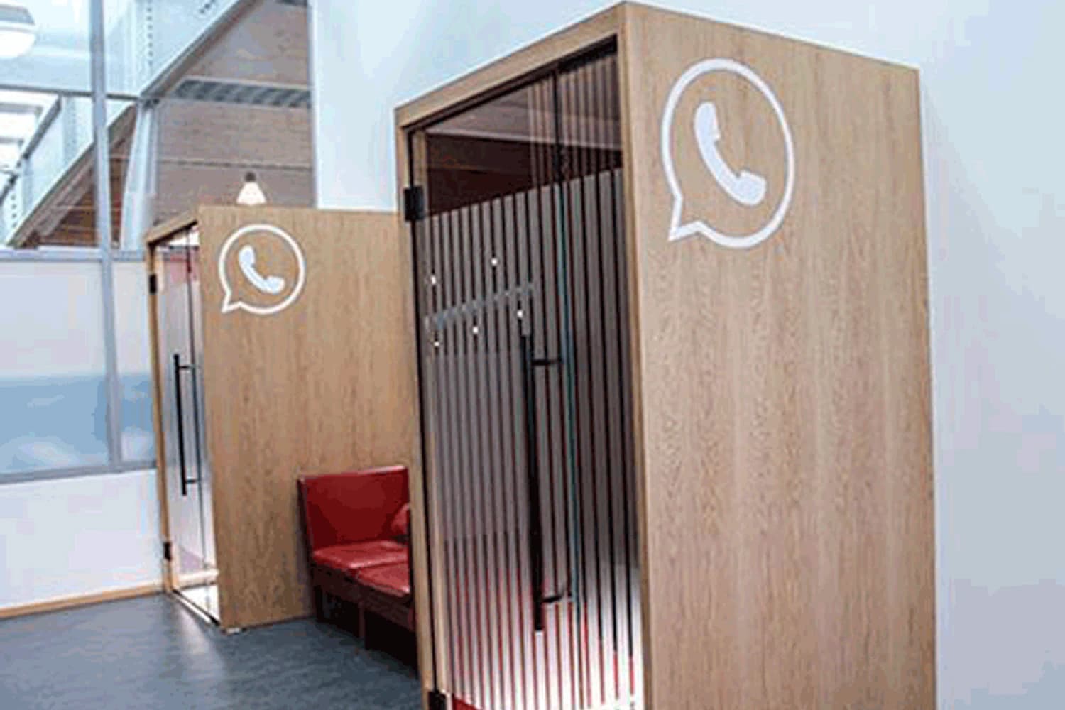 Zwei hölzerne Telefonkabinen mit Glasfront, WhatsApp-Symbol und roten Sitzen innen.