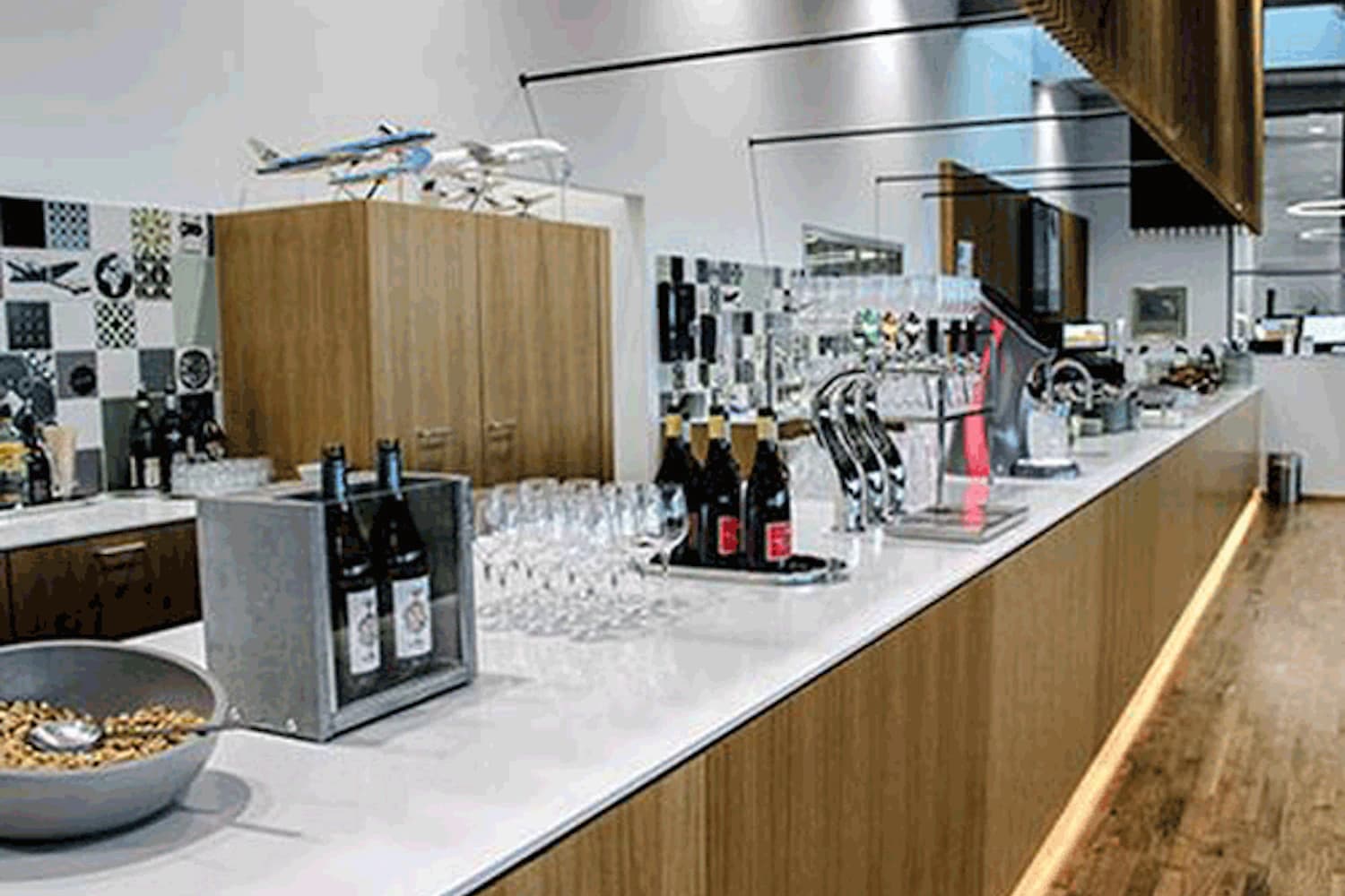 Bar mit Weinflaschen, Gläsern und Zapfhähnen vor Holzschränken in der King Amlet Lounge am Flughafen Billund