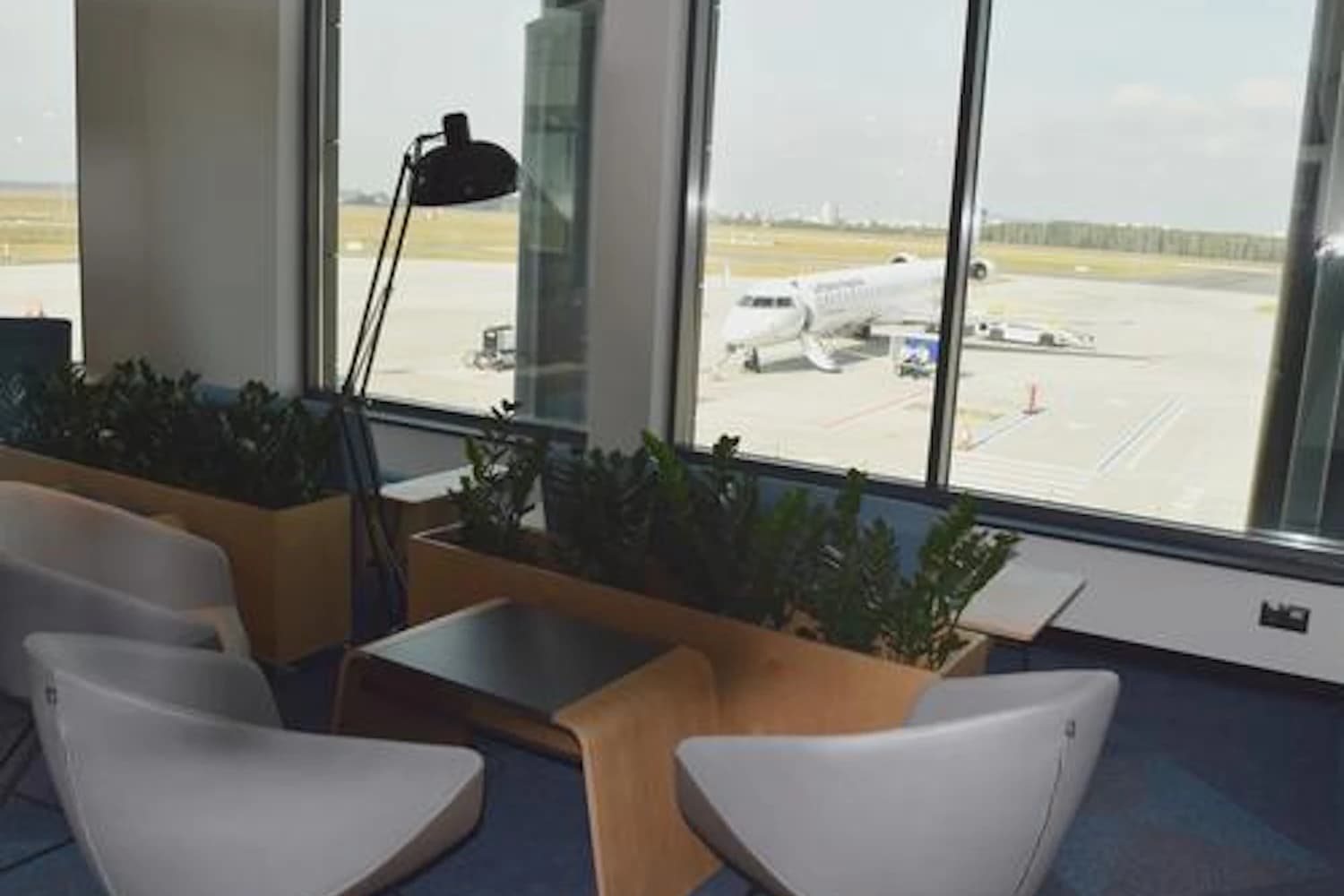 Stühle und Tische vor den großen Fenstern der Executive Lounge am Flughafen Bydgoszcz mit Flugzeug auf dem Vorfeld