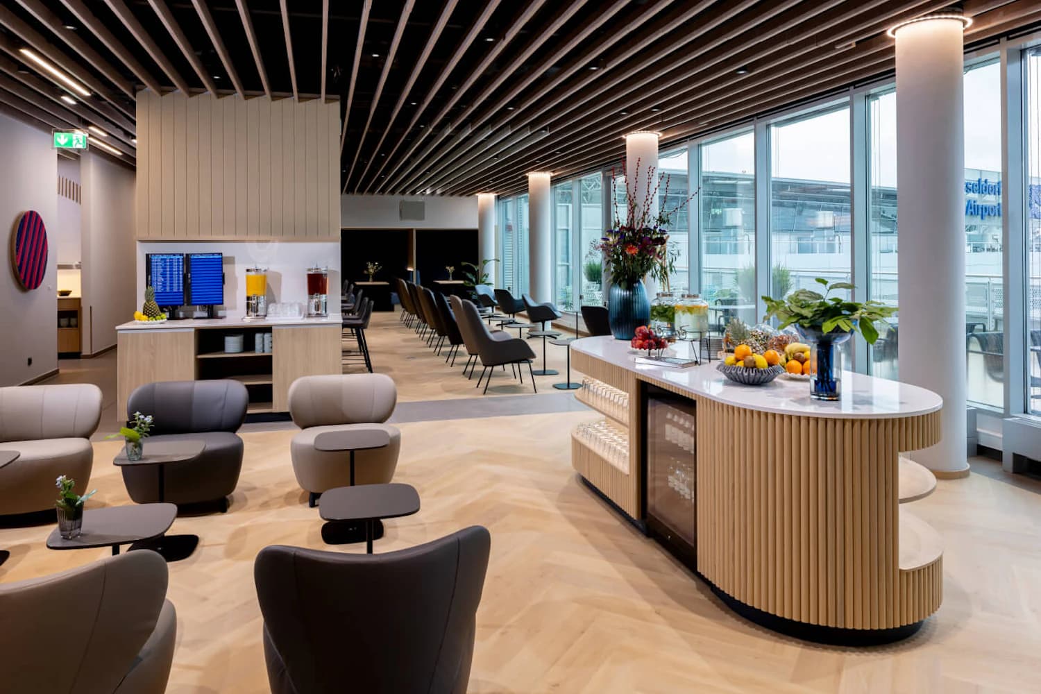 Helle Lounge mit Sitzgruppen, Buffetinsel und großen Fensterfronten zum Flughafenvorfeld.