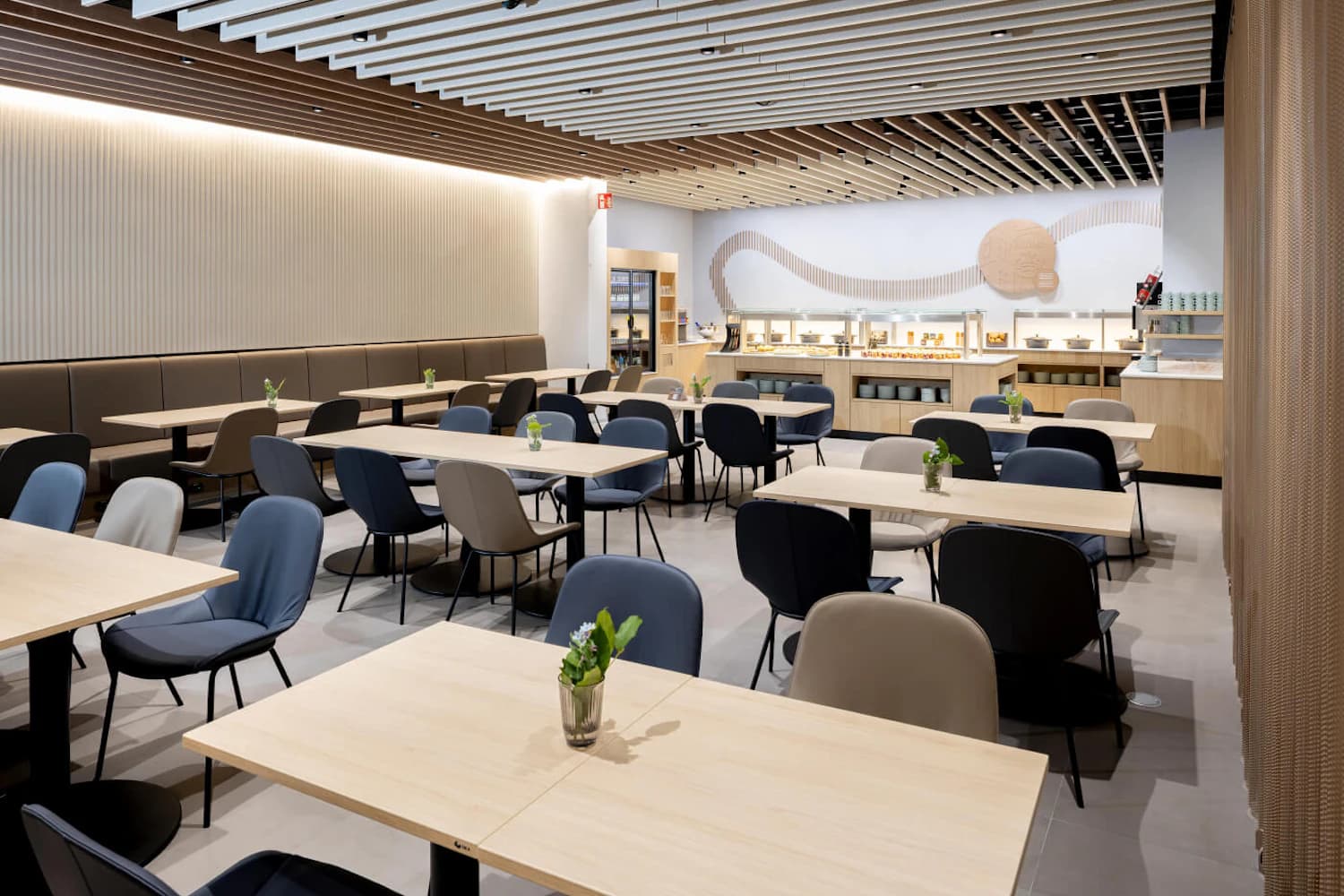 Leerer Loungebereich mit mehreren Tischen, gepolsterten Stühlen, Buffet an der Rückwand und Holzlamellendecke.