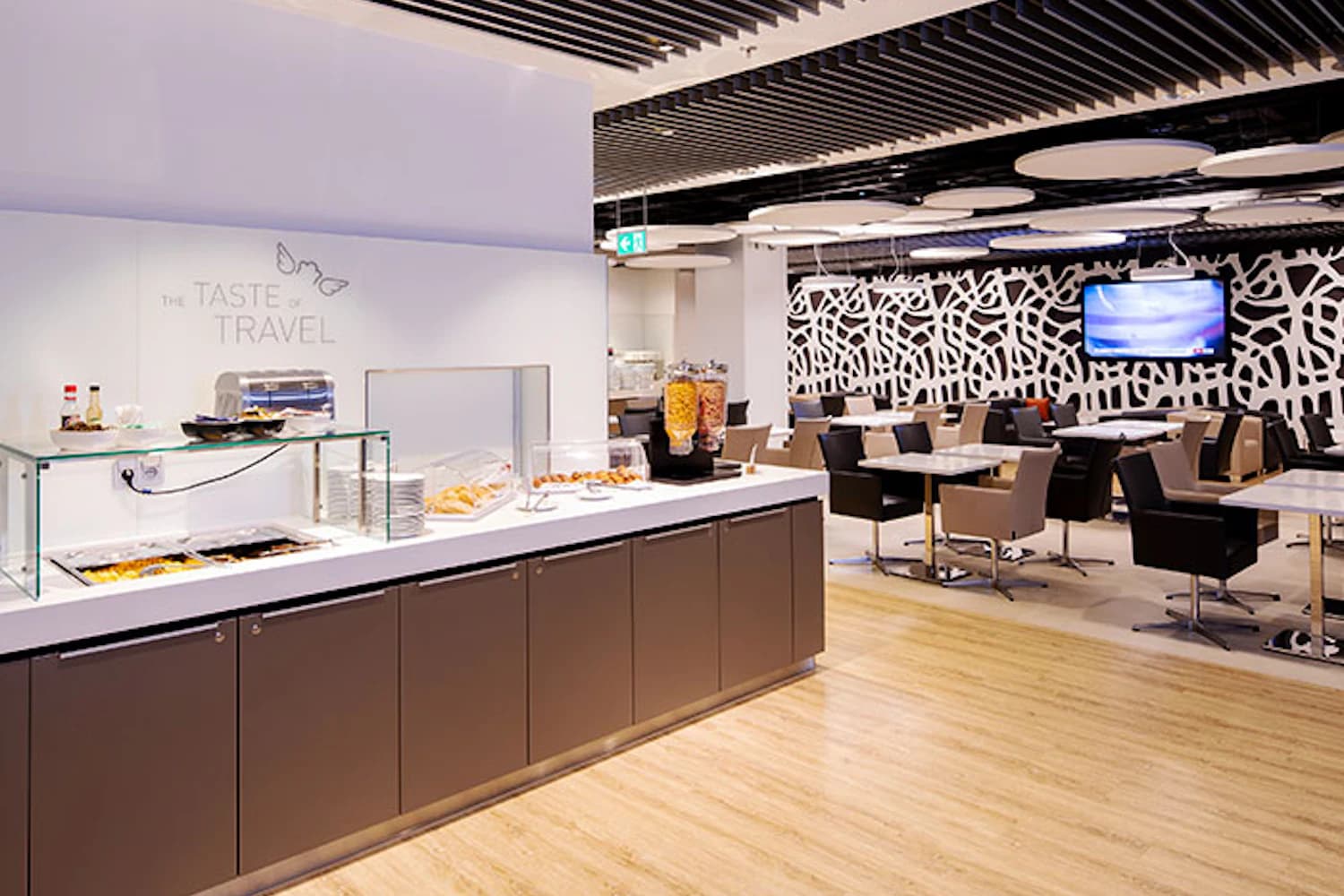Moderner Ruhebereich mit Buffettheke, Getreidespendern und mehreren Sitzgruppen in einer Flughafenlounge.
