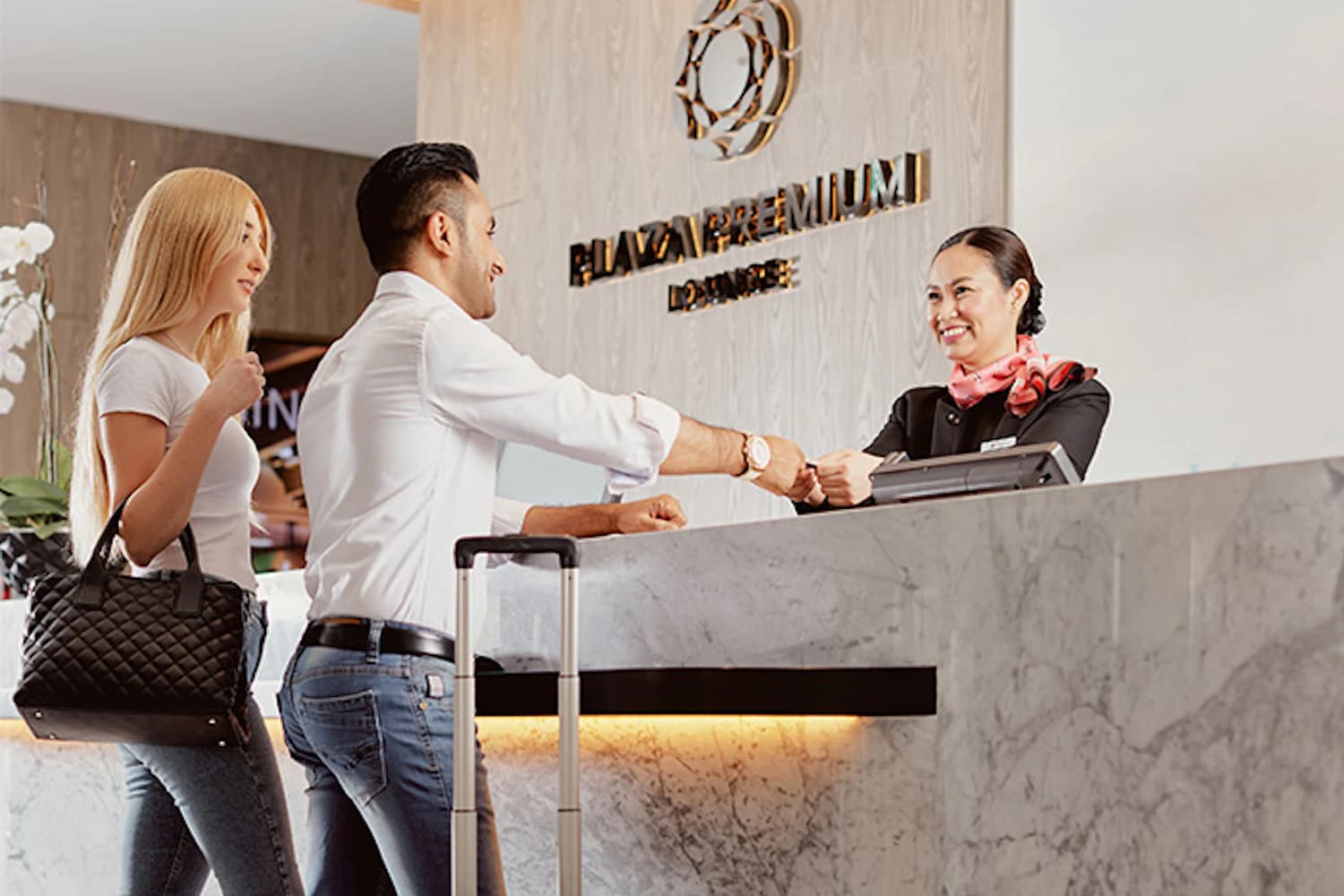 Empfang der Plaza Premium Lounge Dubai mit lächelnder Mitarbeiterin und zwei ankommenden Gästen