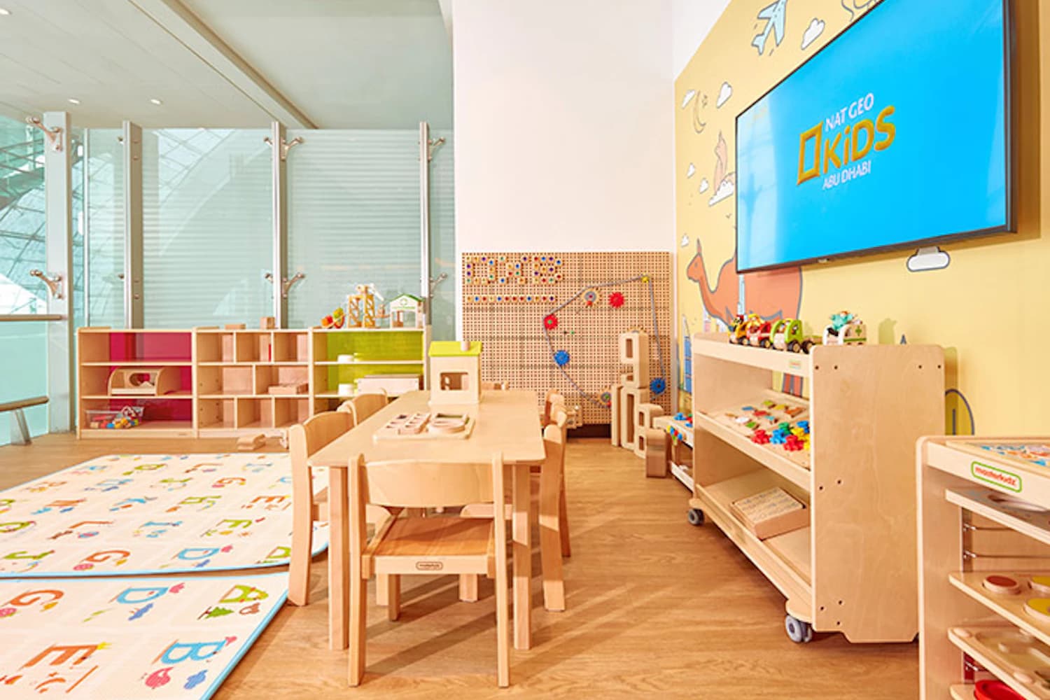Kinderbereich mit Holztisch, kleinen Stühlen, Spielregalen und bunten Matten in der Plaza Premium Lounge Dubai