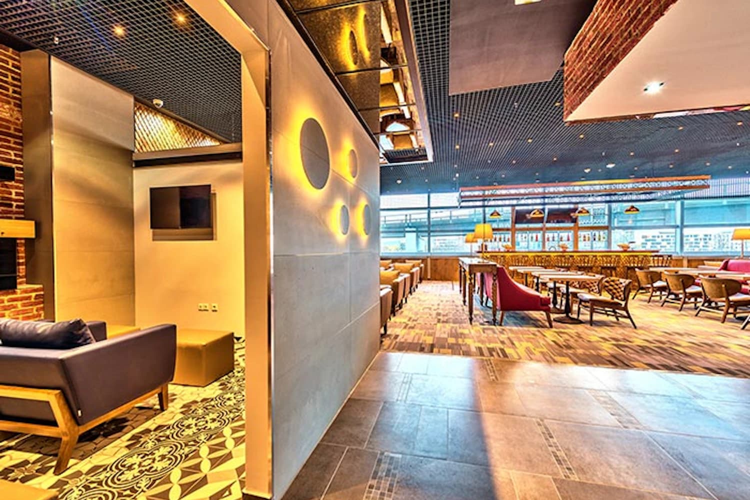 Lounge mit verschiedenen Sitzbereichen, Tischen und großen Panoramafenstern am Flughafen.