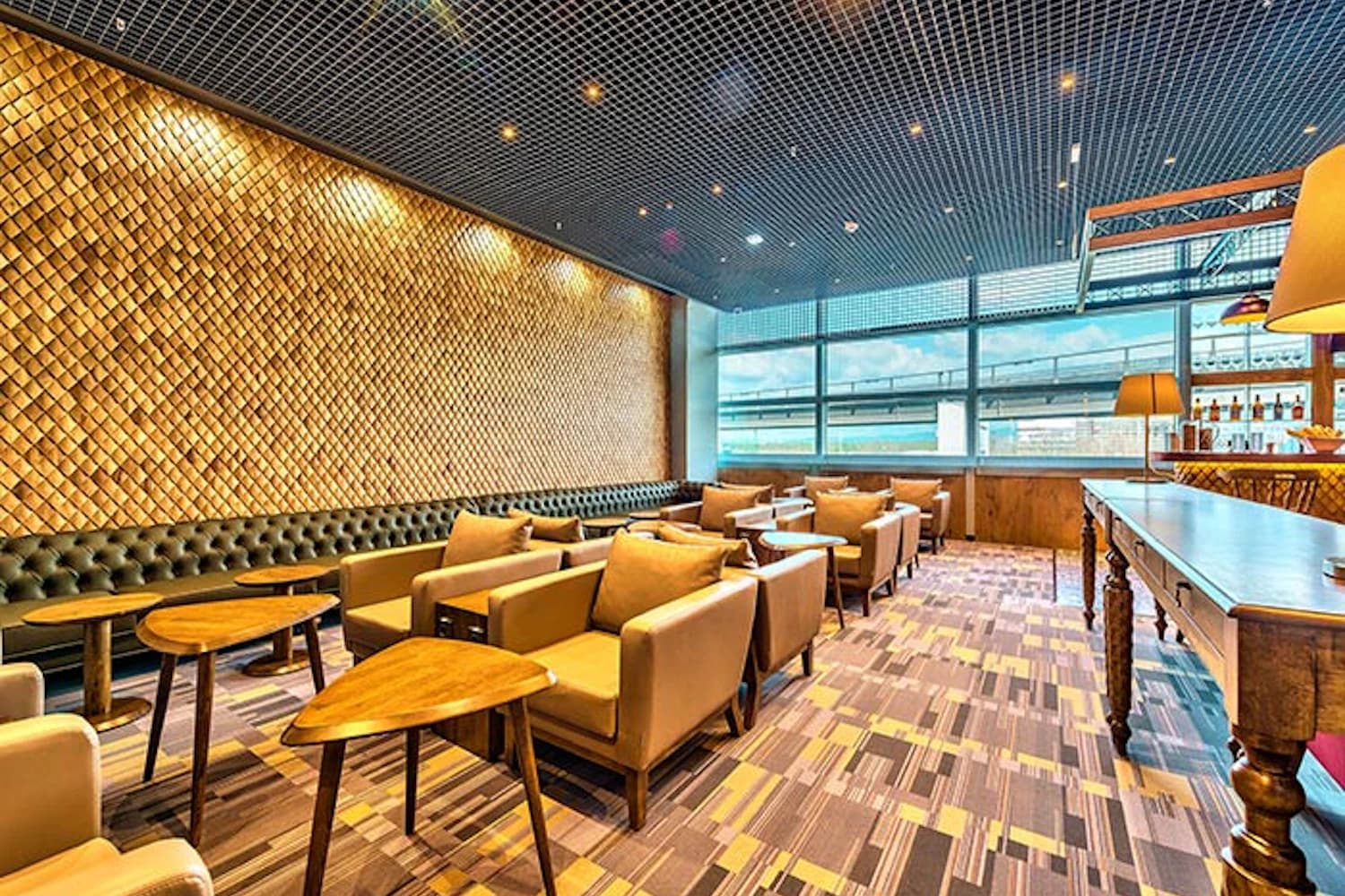 Hellbraune Sessel mit kleinen Holztischen vor den Fenstern zum Rollfeld in der Primeclass Lounge am Flughafen Frankfurt