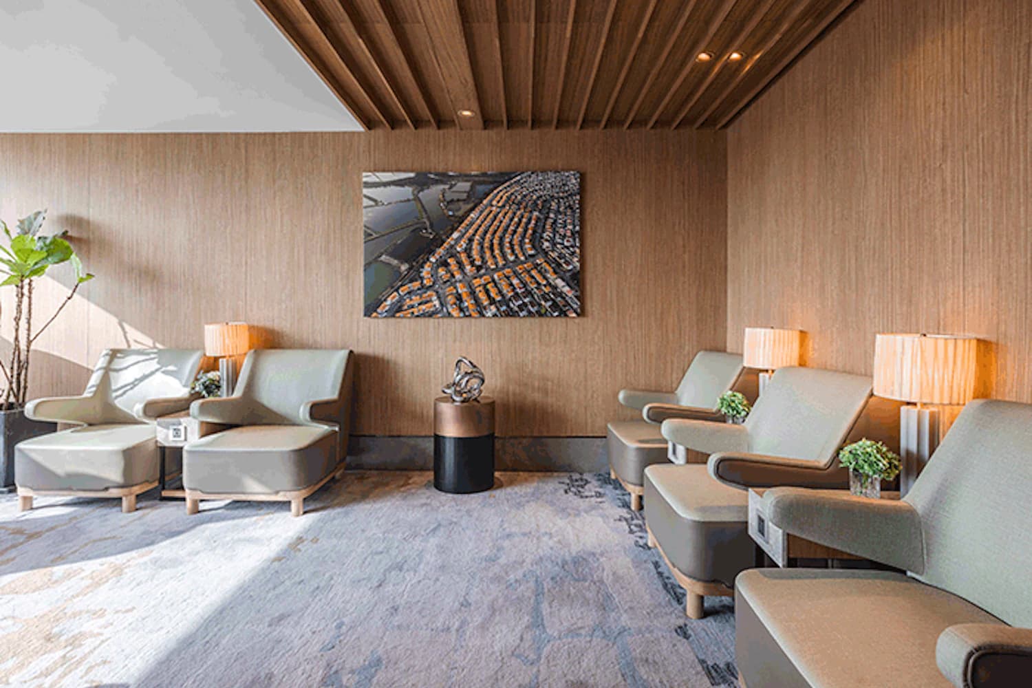 Helle Lounge mit mehreren Sesseln, Beistelltischen, Stehlampen, Teppichboden und Holzwand.