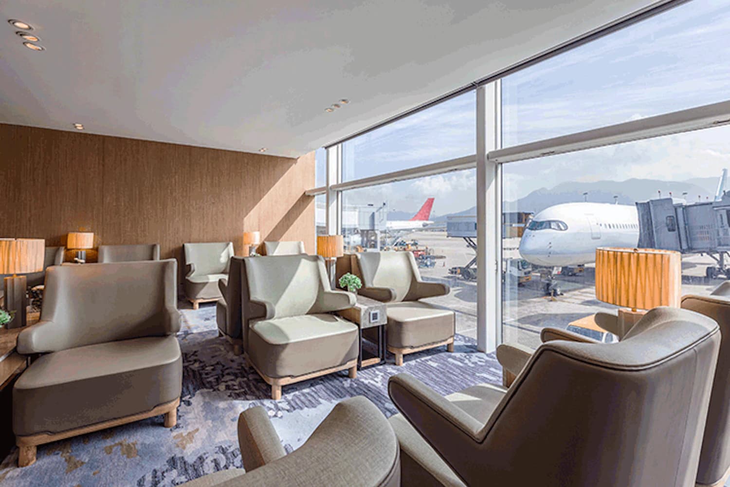 Sessel vor bodentiefen Fenstern mit Blick auf ein Flugzeug am Gate in der Plaza Premium Lounge Gate 35 am Flughafen Hongkong