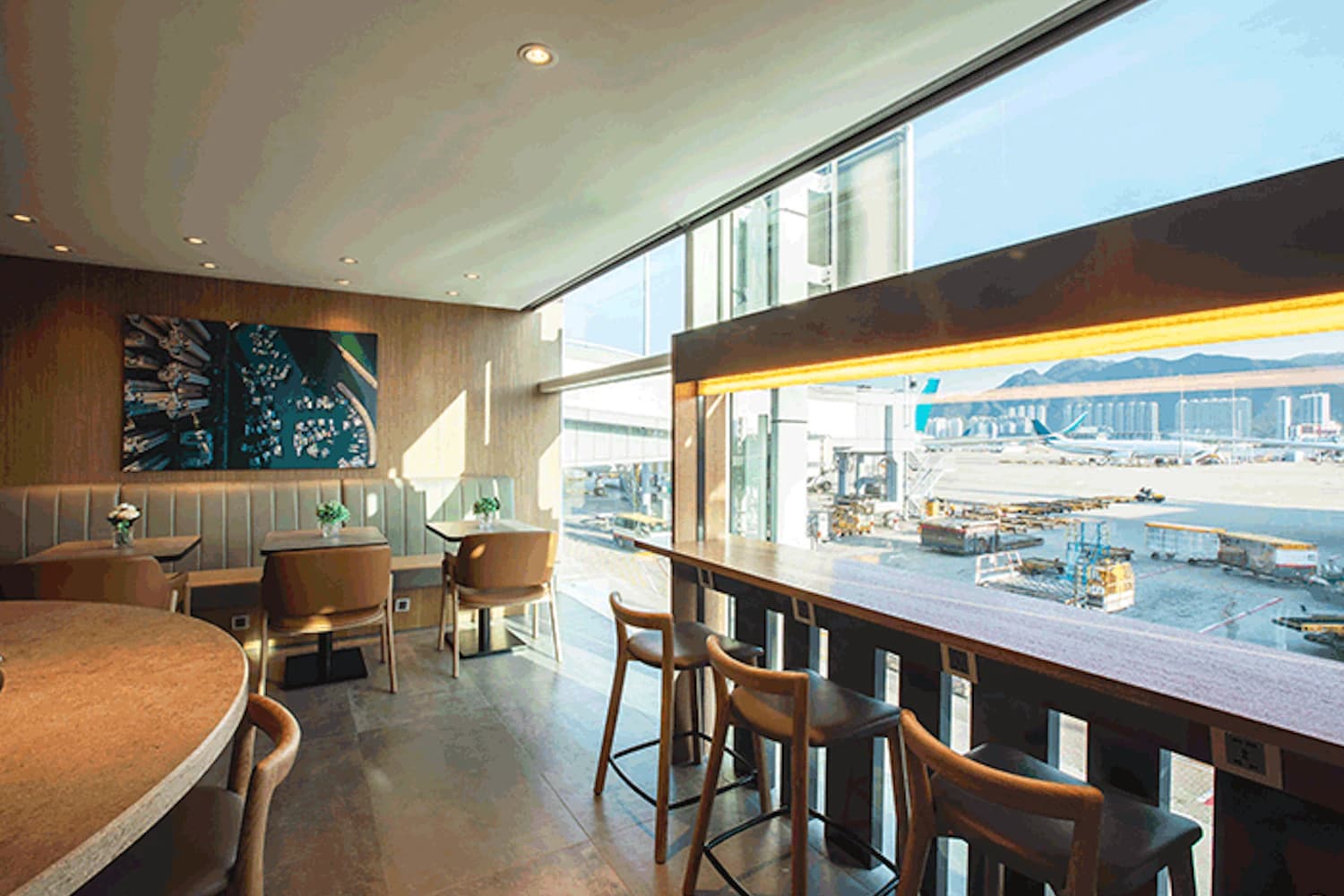 Helle Flughafenlounge mit Sitzplätzen, Fensterbank und Blick auf Rollfeld und abgestelltes Flugzeug.