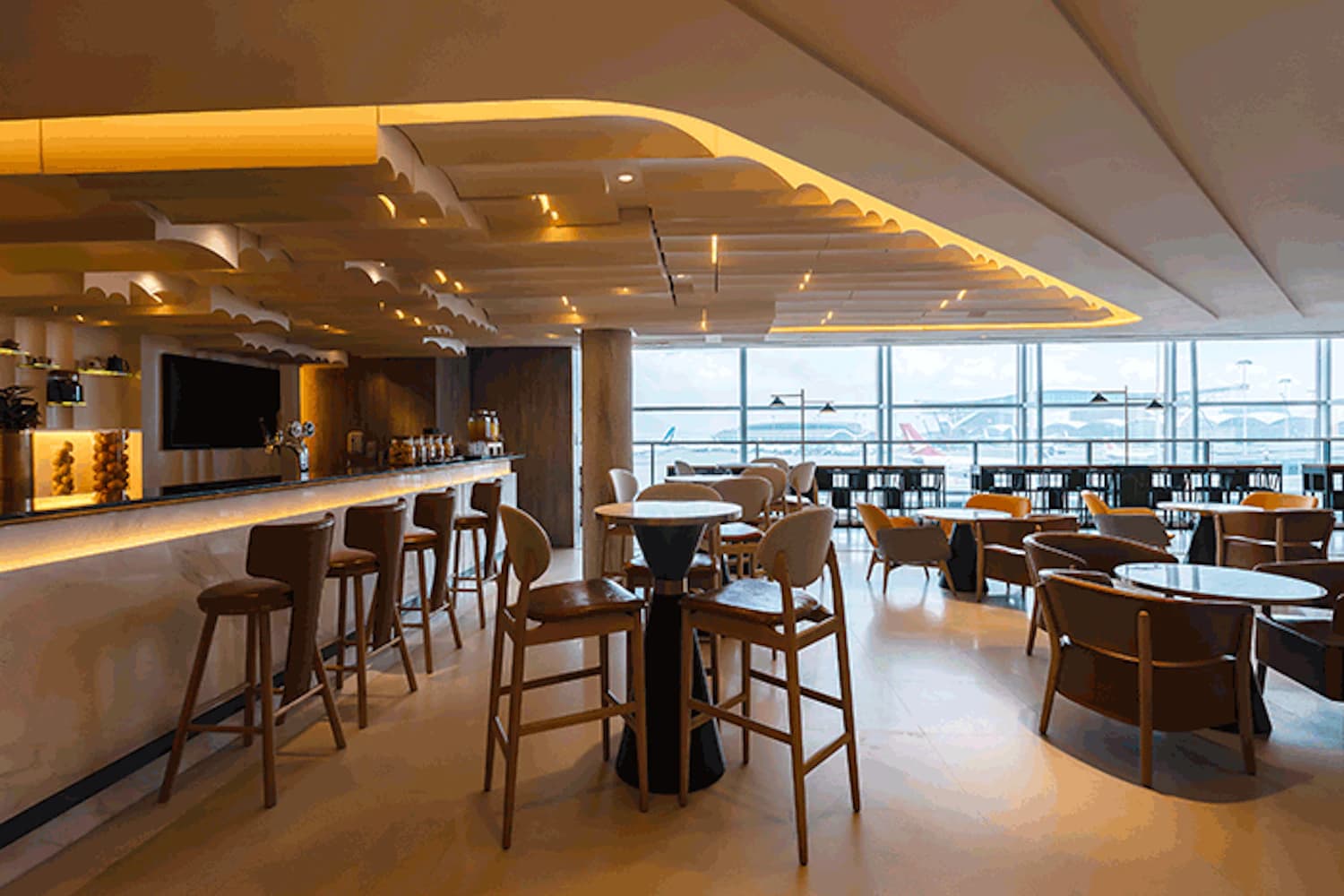 Loungeinneneinrichtung mit Bar, hohen Stühlen, Tischen und großen Fensterfronten zum Flugfeld.