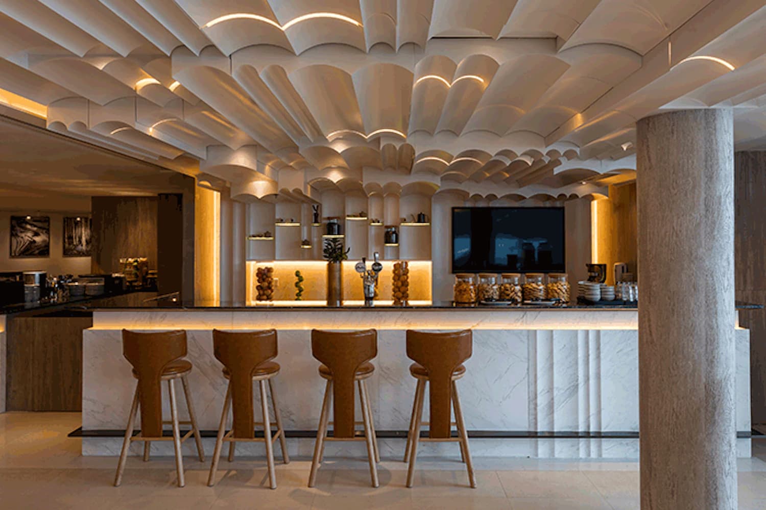 Barbereich in Lounge mit Marmortheke, fünf Barhockern, dekorativen Gläsern und gewölbter Decke mit indirekter Beleuchtung.