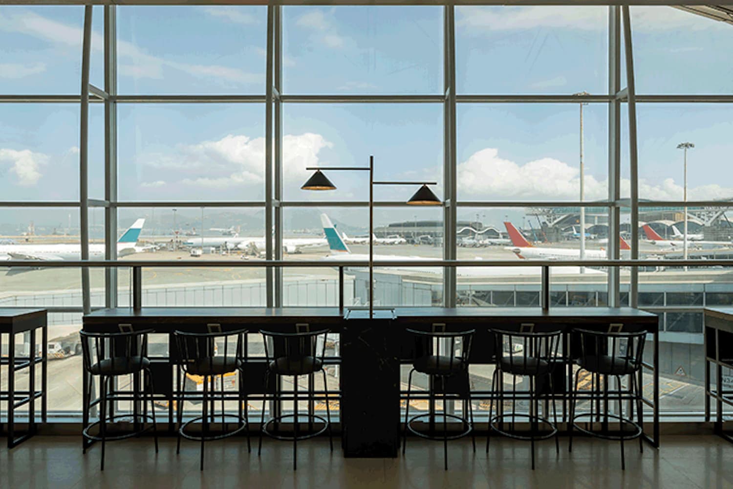 Reihenhohe Fenster mit Barhockern und Tischen, Blick auf Flugzeuge am Vorfeld eines Terminals.