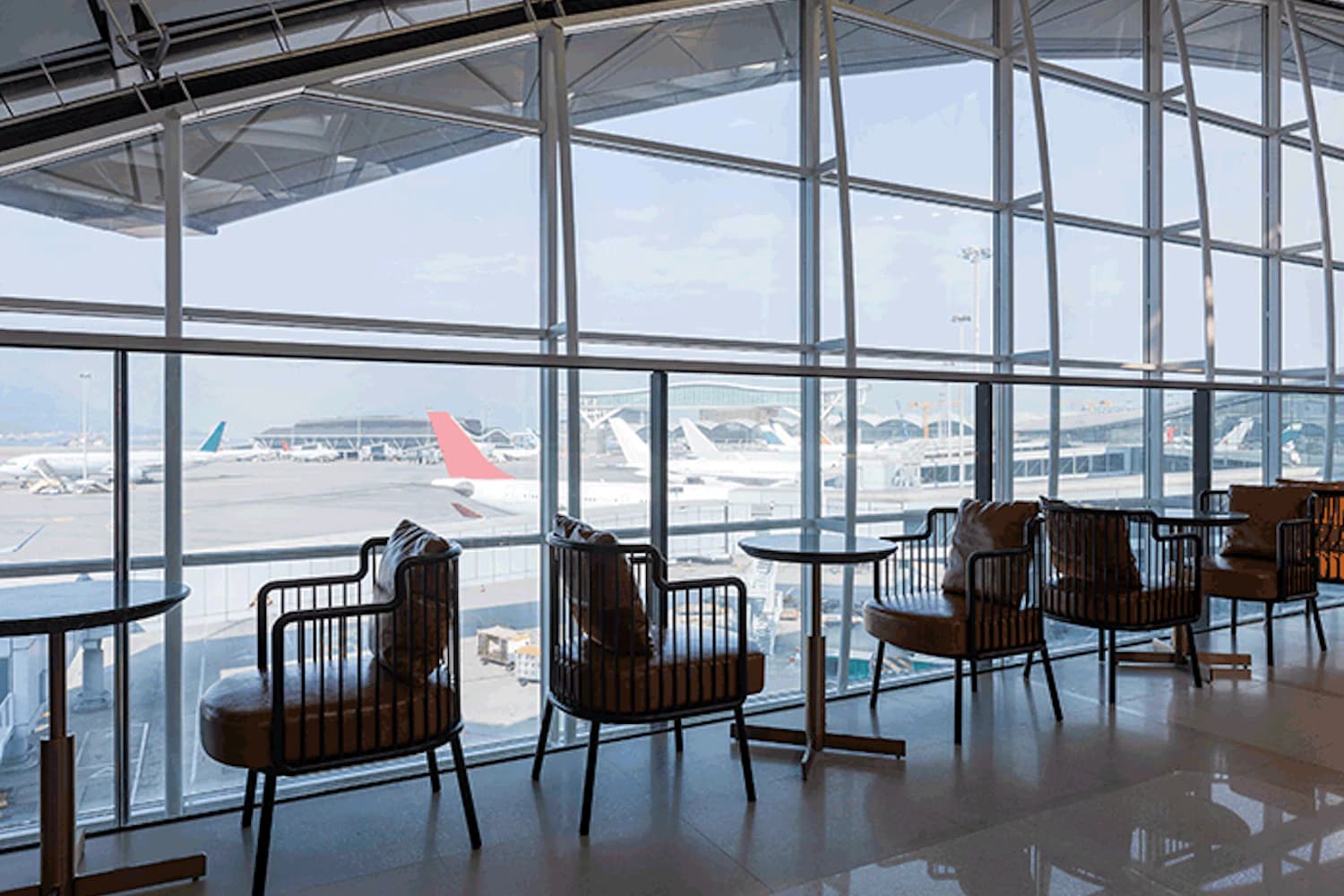 Reihe bequemer Sessel an den Fenstern der Plaza Premium Lounge Gate 60 am Flughafen Hongkong mit Blick auf geparkte Flugzeuge