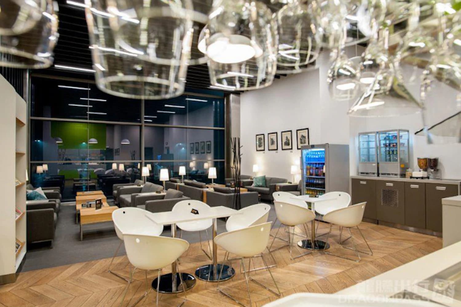 Weiße Stühle an Tischen, Sofas und Getränkekühlschrank in der Business Lounge am Flughafen Krakau