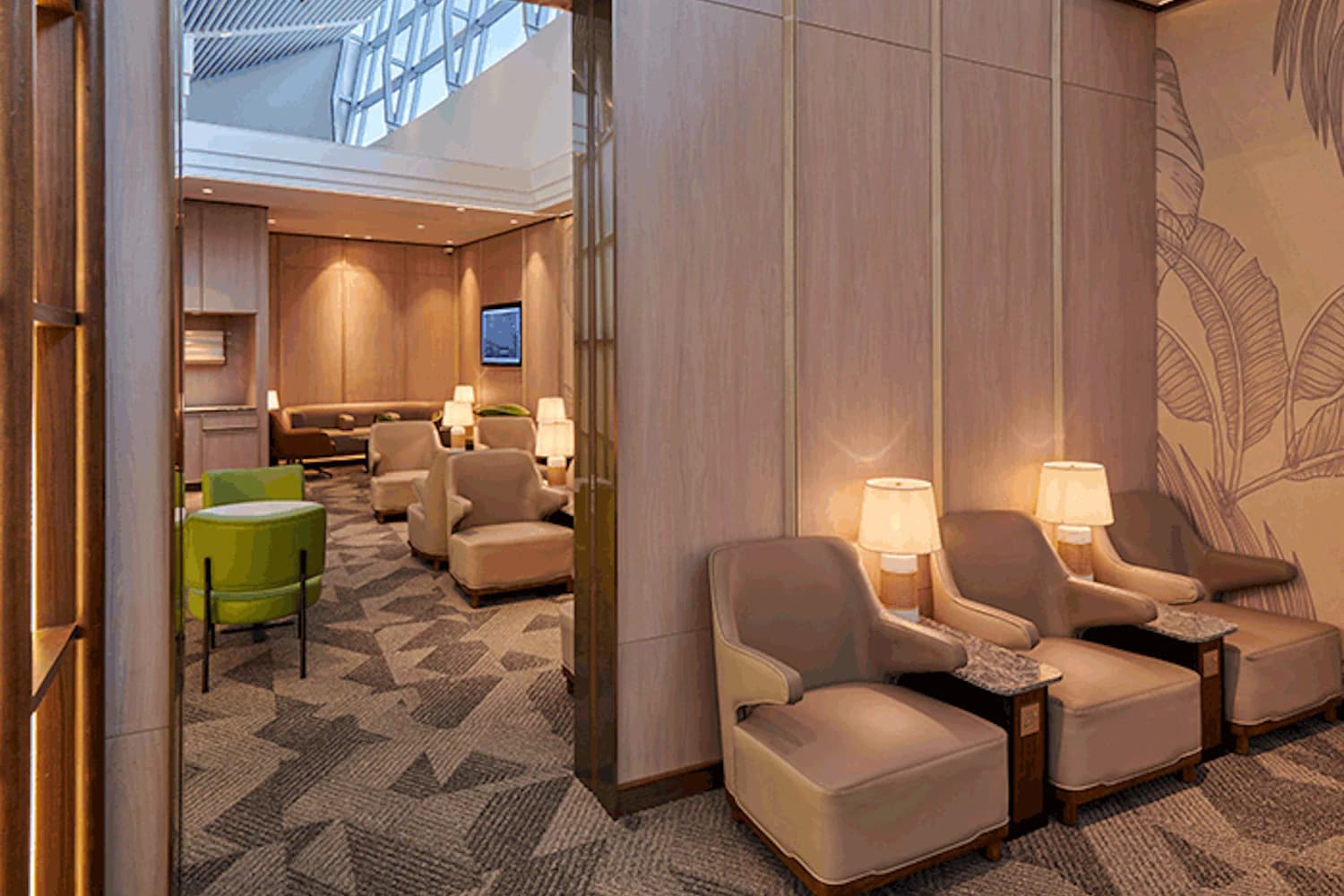 Lounge mit gepolsterten Sesseln, Beistelltischen mit Lampen, Teppichboden und grünen Hockern.