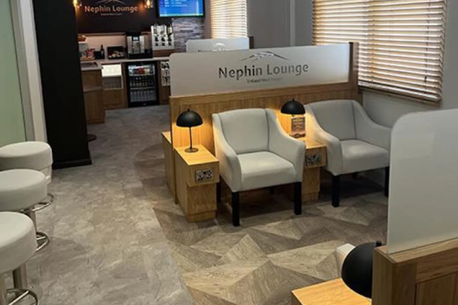 Zwei graue Sessel mit Holztischchen vor der Trennwand mit Nephin-Lounge-Schriftzug am Flughafen Knock