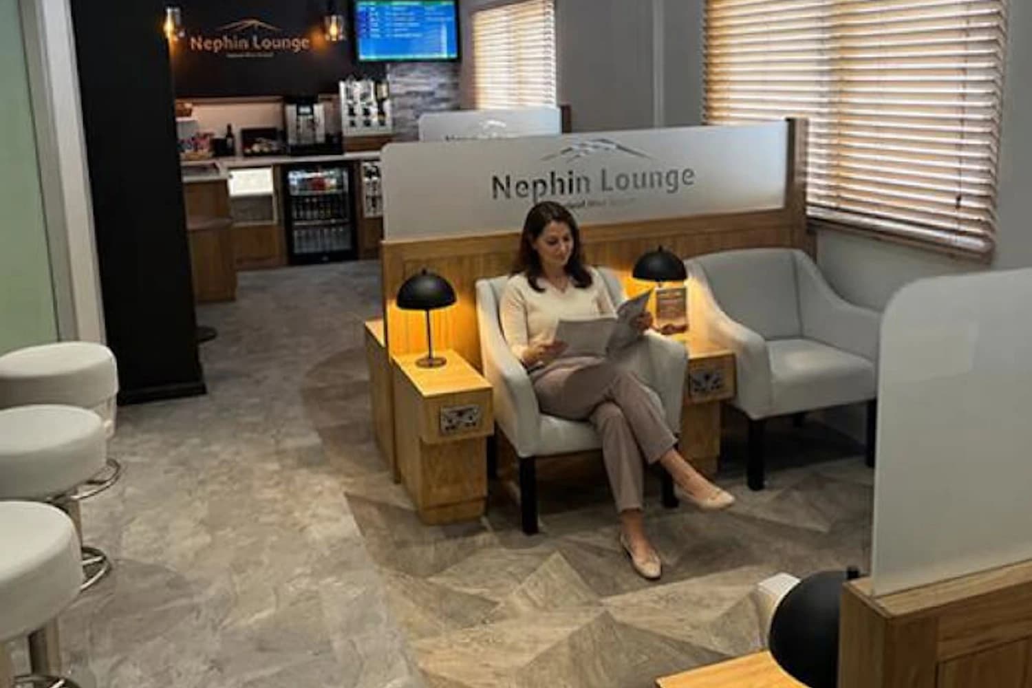 Frau liest in einem Sessel zwischen Sitznischen und Lampen in der Nephin Lounge am Flughafen Knock