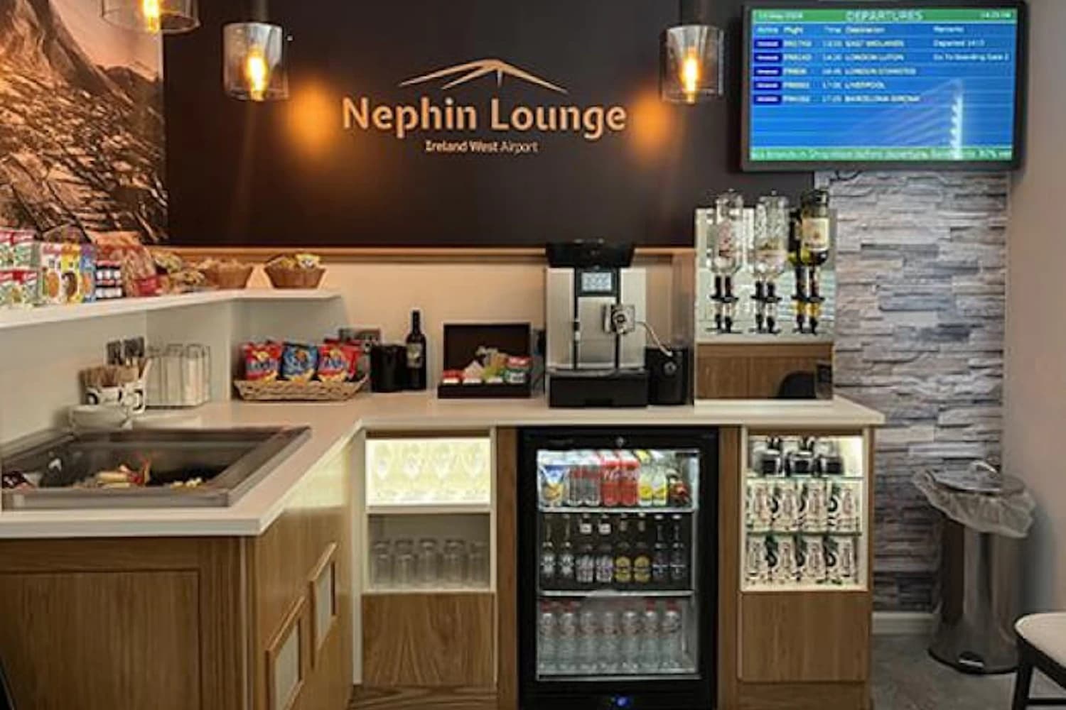 Tresen mit Kühlschrank, Kaffeemaschine, Snacks und Abfluganzeige in der Nephin Lounge am Flughafen Knock
