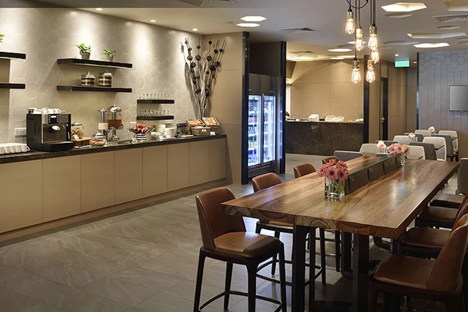Selbstbedienungsbuffet mit Kaffeemaschine und langem Holztisch in der Plaza Premium Lounge am Flughafen Singapur