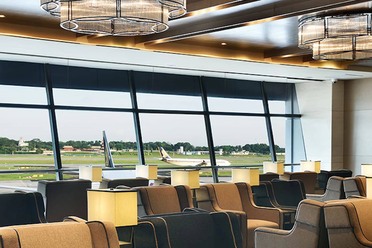 Sessel mit Tischlampen vor den Fenstern zum Rollfeld in der Plaza Premium Lounge am Flughafen Singapur