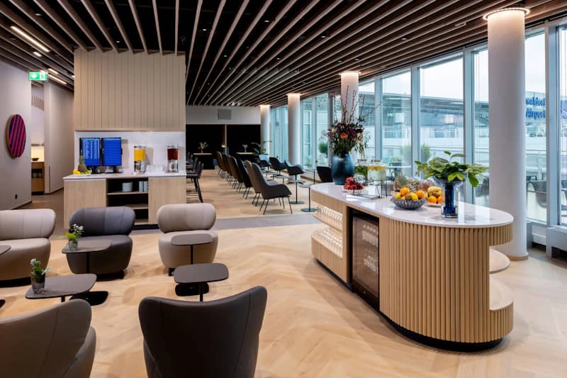 Helle Lounge mit Sitzgruppen, Buffetinsel und großen Fensterfronten zum Flughafenvorfeld.