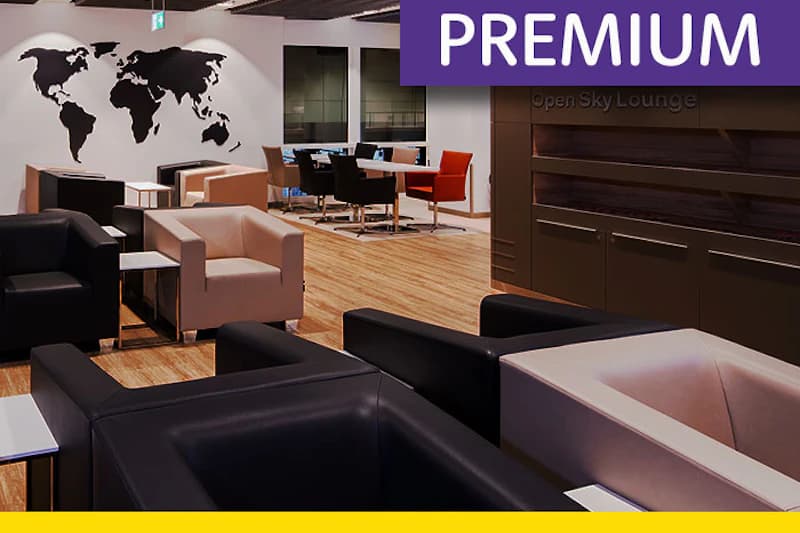 Lounge mit schwarzen und beigen Sesseln, Holzboden, Tischen und Weltkartenmotiv an der Wand.