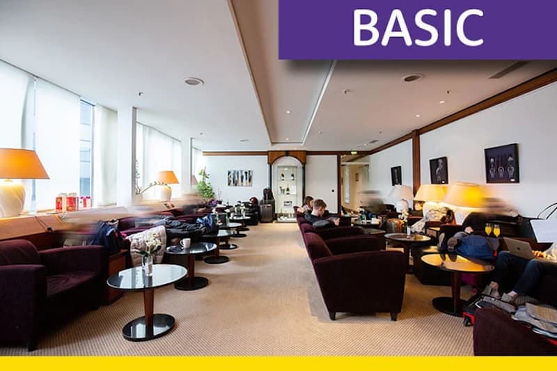 Lounge mit Reihen dunkelvioletter Sessel, runden Beistelltischen, Stehlampen und großen Fensterfronten; mehrere Gäste sitzen.